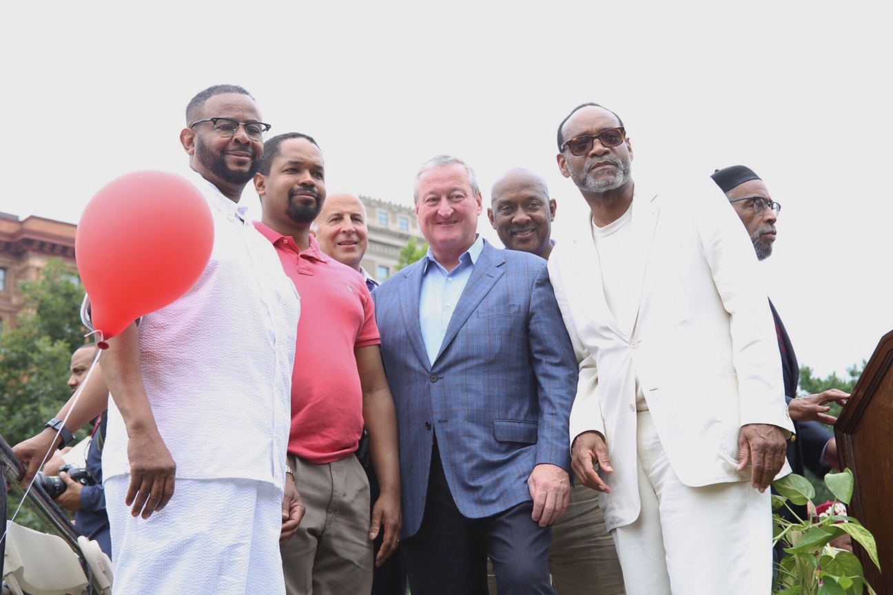 Men stand together wearing business casual attire outside on a cloudy day.