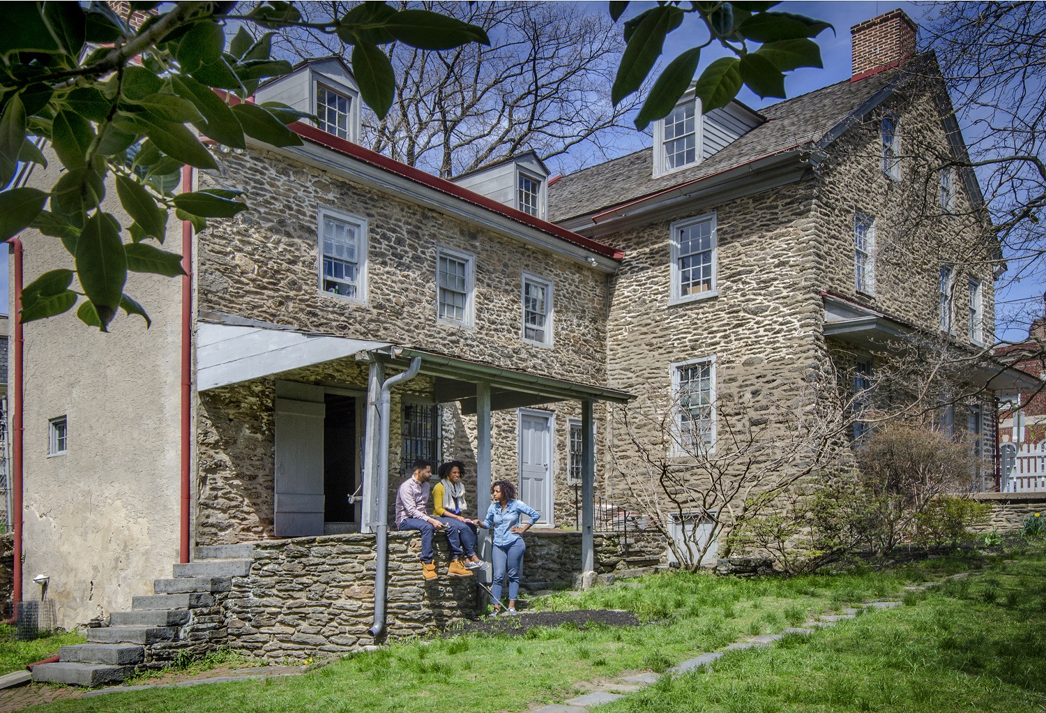 People sit on the porch of a field stone building after taking a tour of the Johnson House.