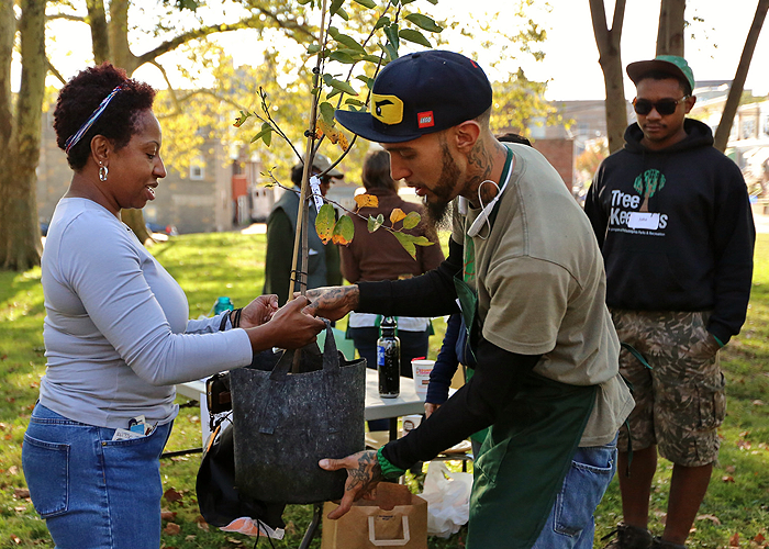 Dos personas sostienen un árbol en una bolsa en un evento del Programa TreePhilly.