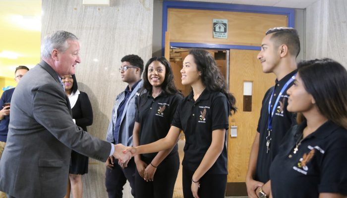 El alcalde Kenney da la mano a los alumnos del instituto George Washington, un centro comunitario, mientras todos sonríen.
