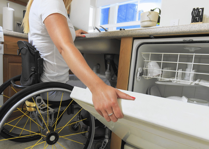 Una mujer en silla de ruedas cierra un lavavajillas.