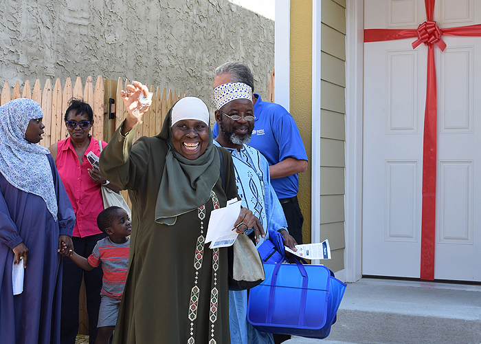 一名妇女微笑着举起钥匙，与家人一起站在她的第一个家的大门口。