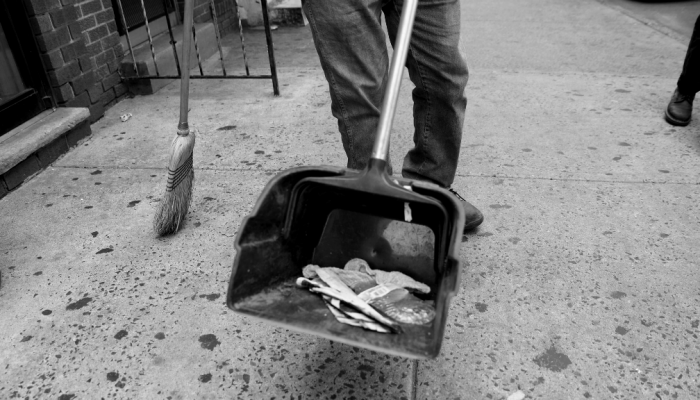 A business owner sweeps up litter into a dust pan in front of his store