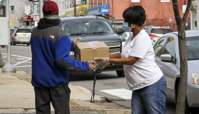 Женщина в маске и перчатках вручает коробку продуктов жителю Филадельфии