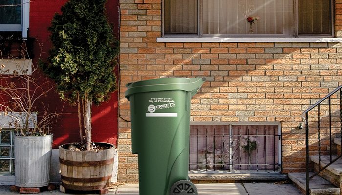Una cesta de basura verde de Philacan en la acera frente a una casa