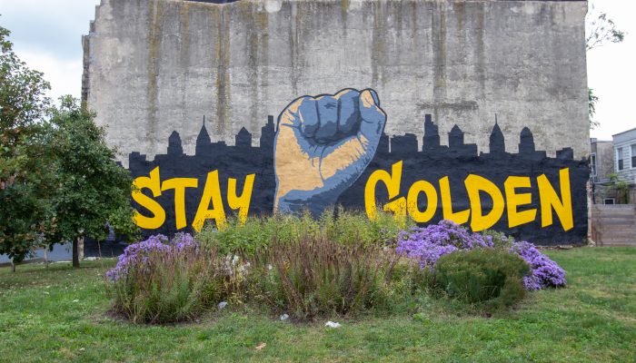 在费城的天际线前有一幅举起拳头的壁画，上面写着：保持金色