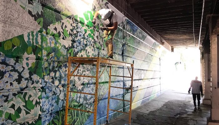 翡翠街壁画、由许多三角形部分的绿色植物画组成。 壁画仍在进行中。 壁画前面有黄色的脚手架，远处站着一个人的剪影。