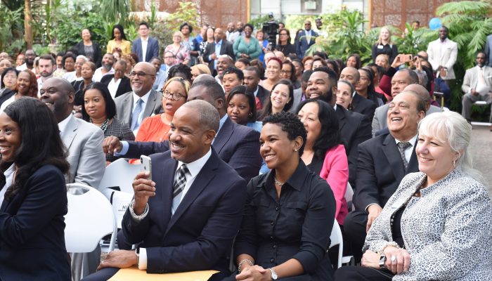 参加少数族裔企业发展周开幕早餐会和颁奖仪式的与会者坐在排椅上，同时微笑着庆祝。