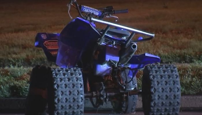 A blue all-terrain vehicle is parked on the roadside in front of a grass field.