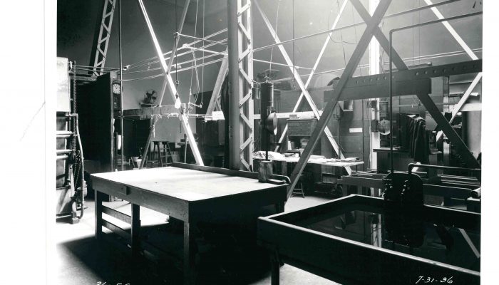 uma fotografia em preto e branco retratando uma grande sala com mesas e equipamentos para o desenvolvimento de filmes