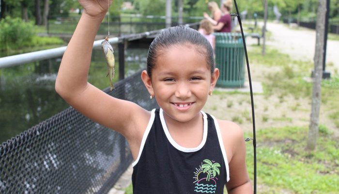 Une jeune fille hispanique sourit en brandissant le poisson qu'elle a pêché dans le cadre de l'un des programmes de pêche gratuits de Philadelphia Parks & Recreation.