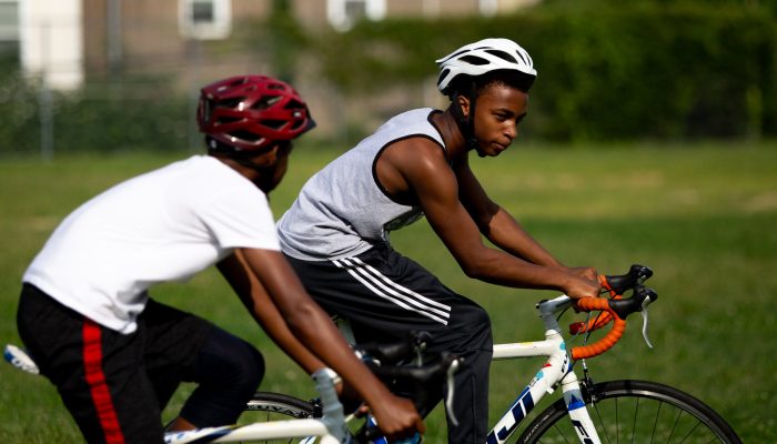 Two African-American boys ride bikes in the park.
