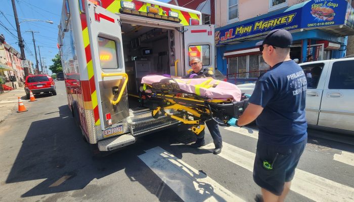 EMT pulls stretcher out of back of ambulance on street in daylight