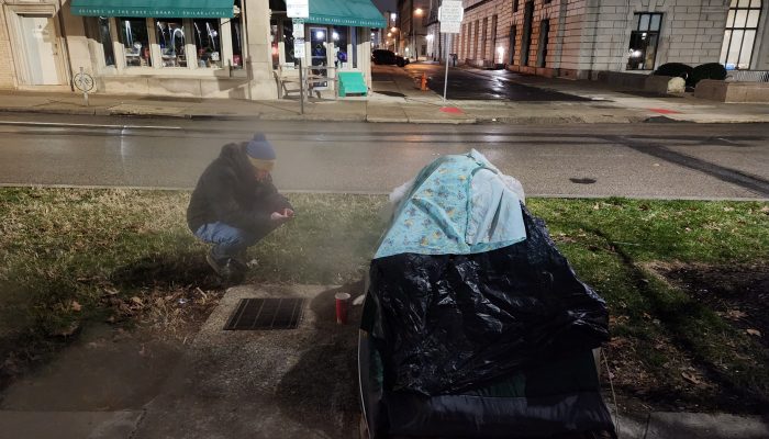 A PIT Count volunteer surveys a person who is living inside a tent on a Philadelphia sidewalk