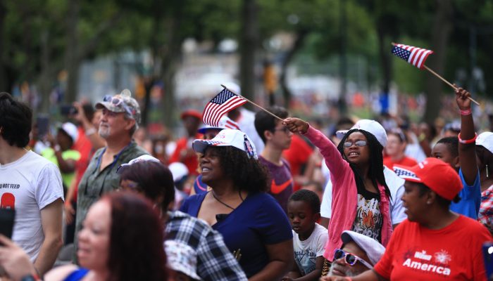 A group of people are smiling and waiving the American Flag at the July 4th Concert
