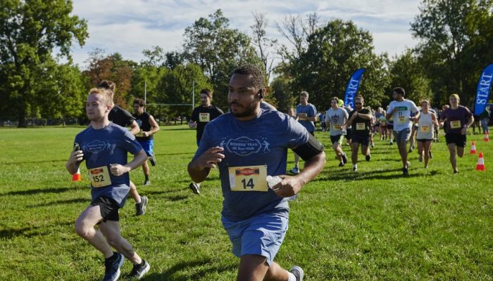 Runners and Walkers take part in the annual Boxers' Trail 5k. An African-American man wearing a blue T-shirt and shorts jogs; there are other runners behind him.