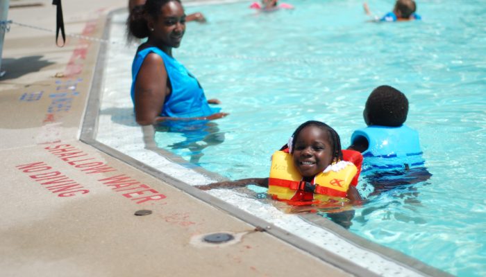 Two children swim in the shallow end of the pool while their mother watches them.