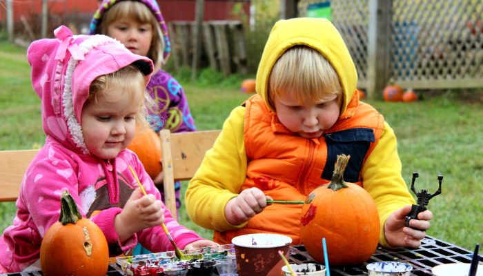 Two young people paint designs on pumpkins.