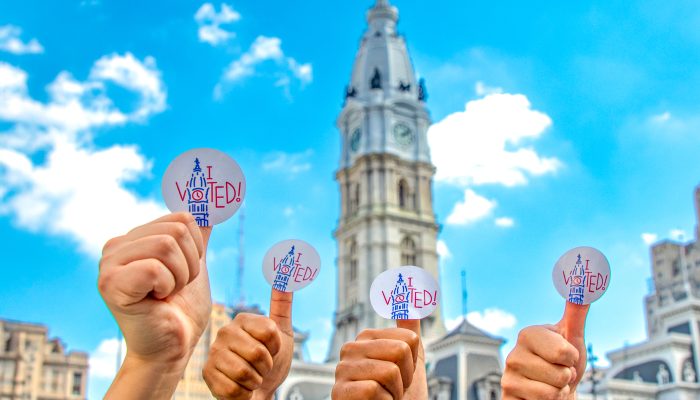 Image of four thumbs holding up "I Voted" stickers