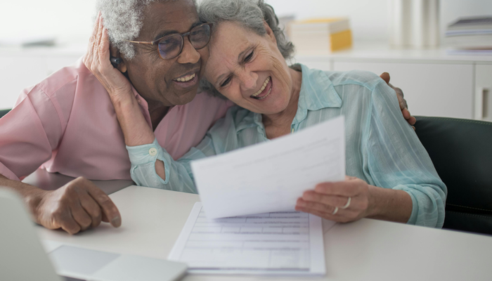 Two older adults smile as they look through paperwork.