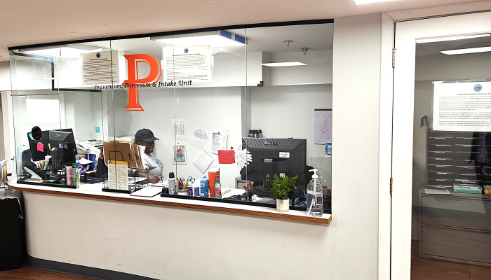 Staff member shown inside RDC intake center seated at a computer, visible through a big glass window marked "Prevention, Diversion & Intake"