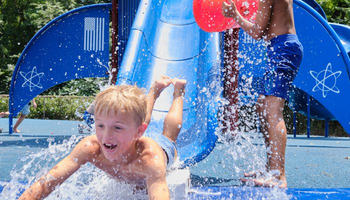 A young person slides down a water slide at camp.