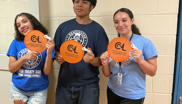 Three young people stand together and hold signs that read 